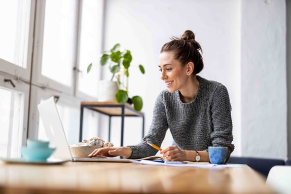 A female sits at a table with her laptop open and coffee sitting next to her.
