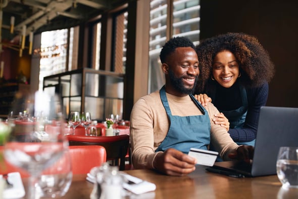 Restaurants owners sit at a table and use a credit card on a computer.