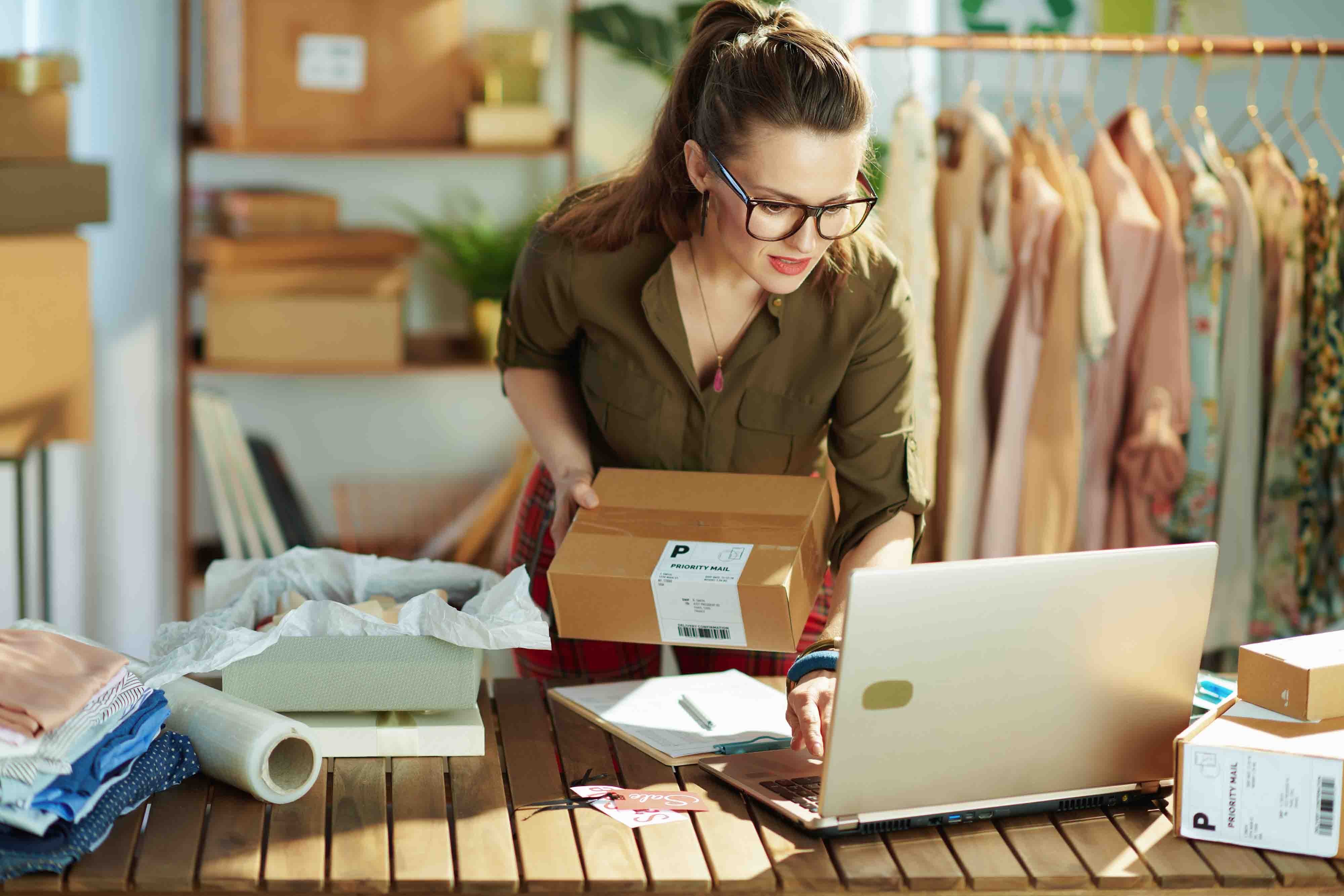 A woman stands in her clothing shop at her computer printing shipping labels.