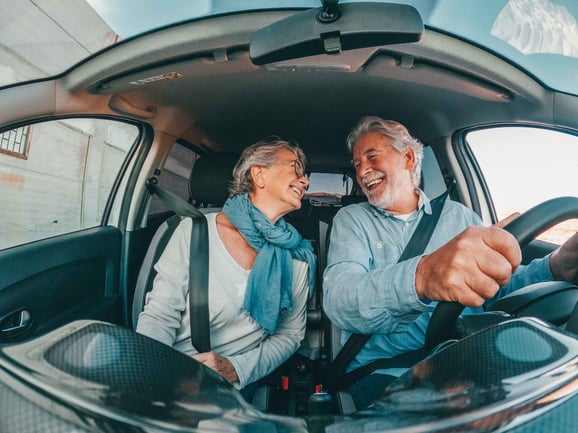 A man and female sit in the front seat of a car looking at each other.