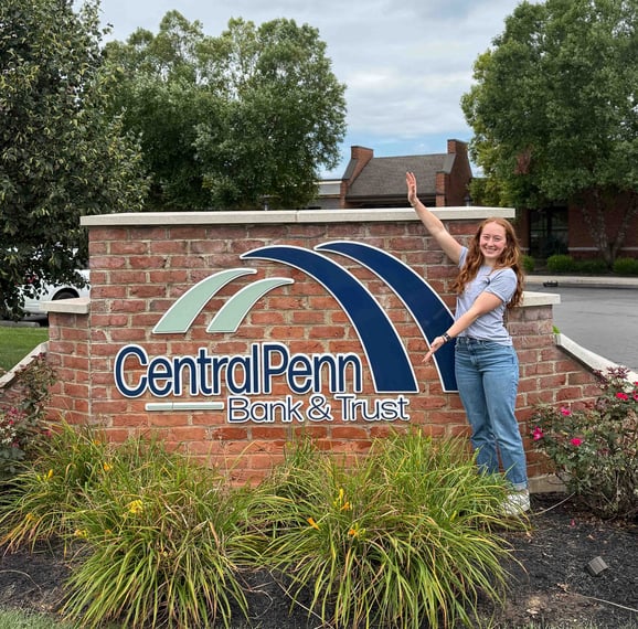 Central Penn employee stands in front of the logo sign with her arms stretched out.