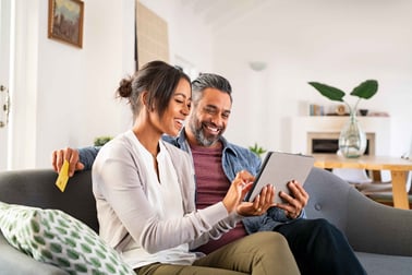Couple sits on couch together looking at a tablet.