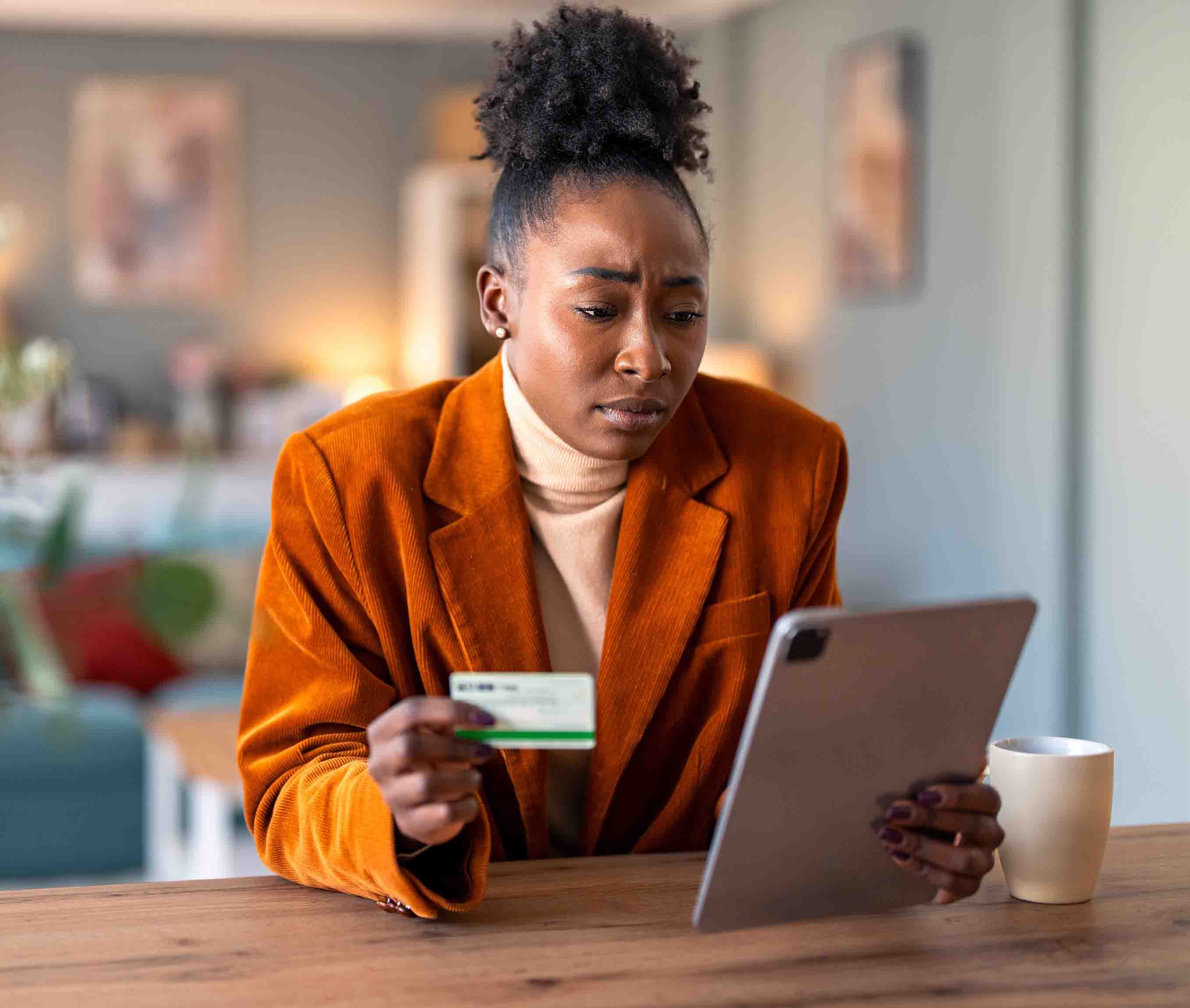 A female sits at a table with a tablet in one hand and her debit card in the other.