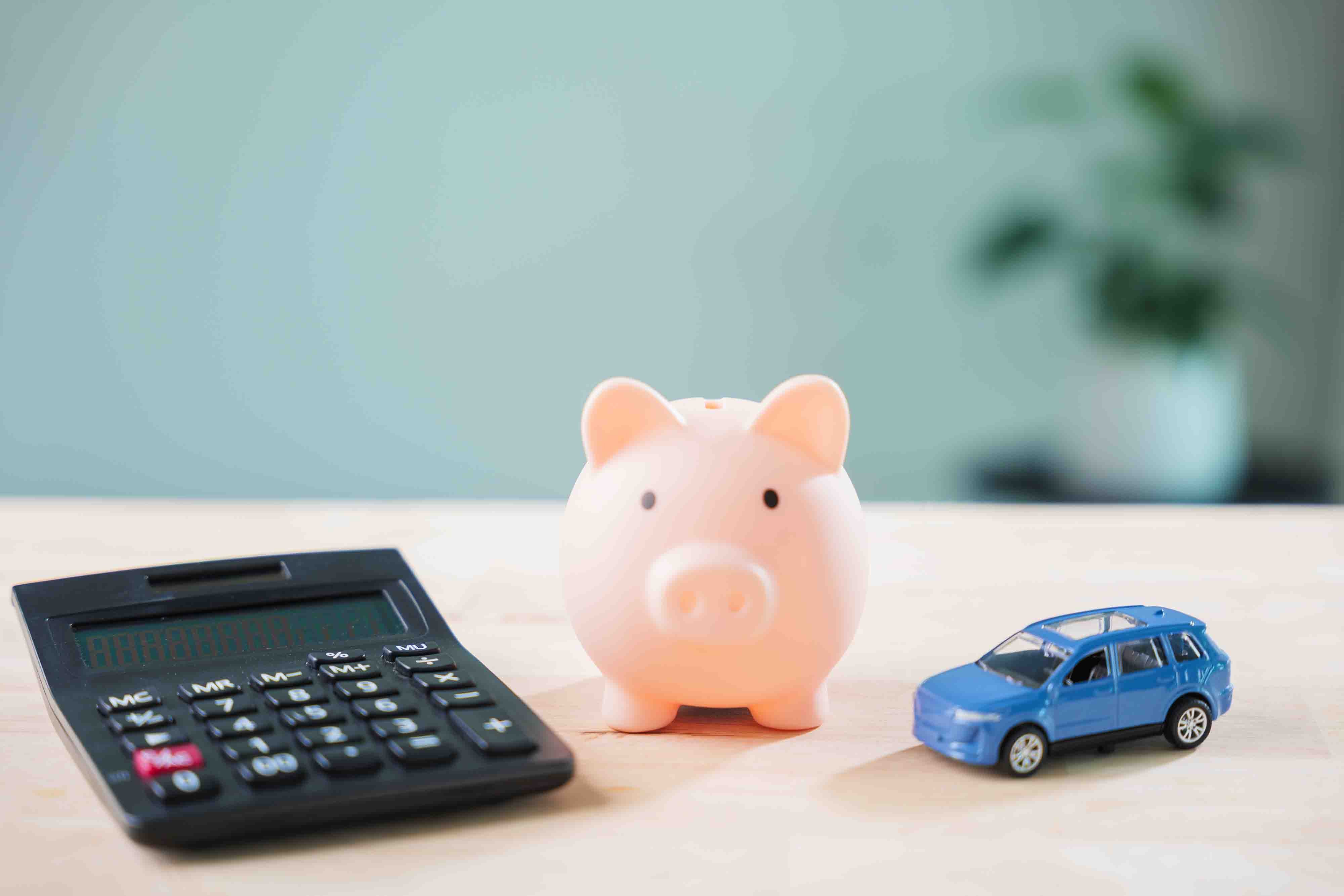 A calculator, a piggy bank, and a toy card sit on a table.