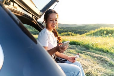 A girl sits in the back of her car after a hike on her phone.
