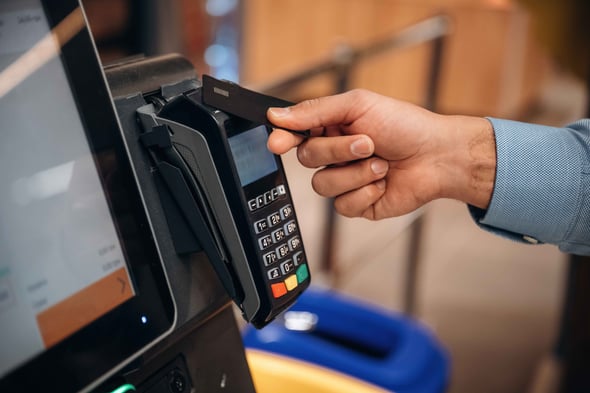 A mans hand uses a credit card to tap to pay at a kiosk.