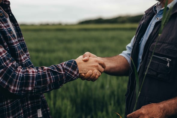 Two men stand in a field shaking hands.