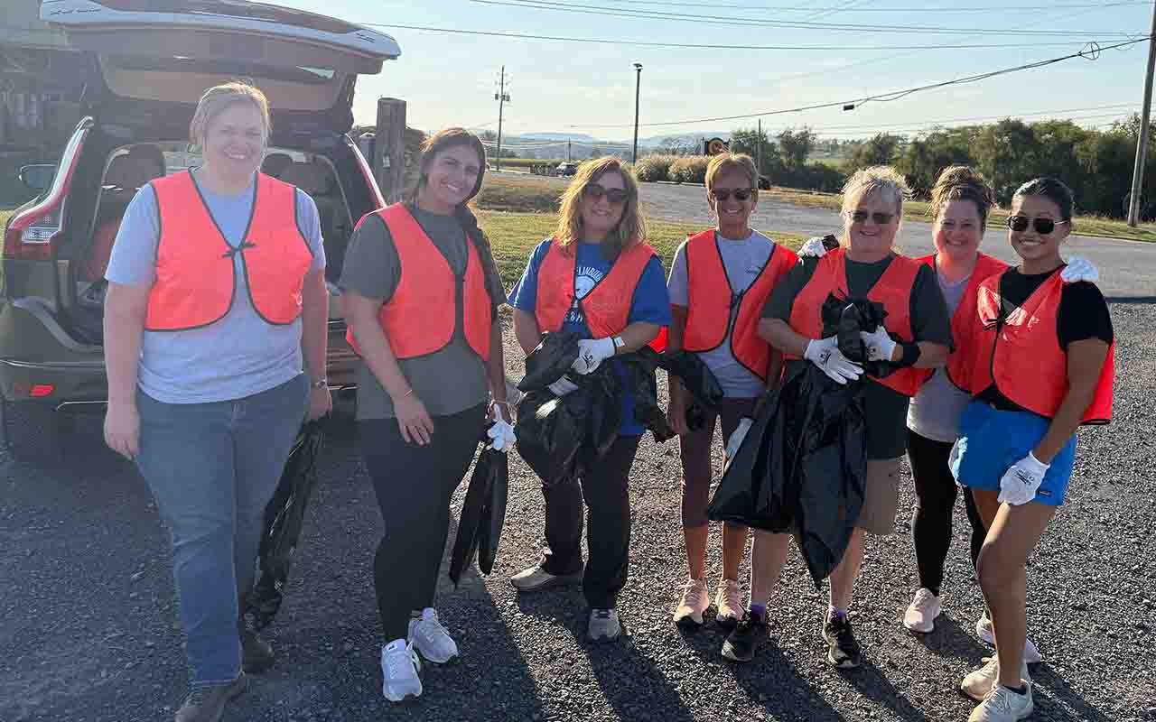Seven Central Penn Bank employees stand with orange vests geared up for highway cleanup.