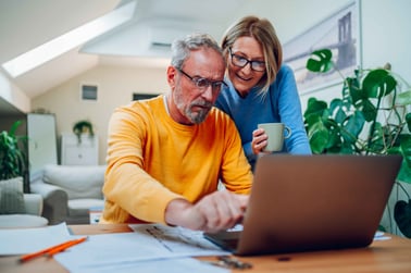 A man and woman sitting a table reviewing their finances on a computer.