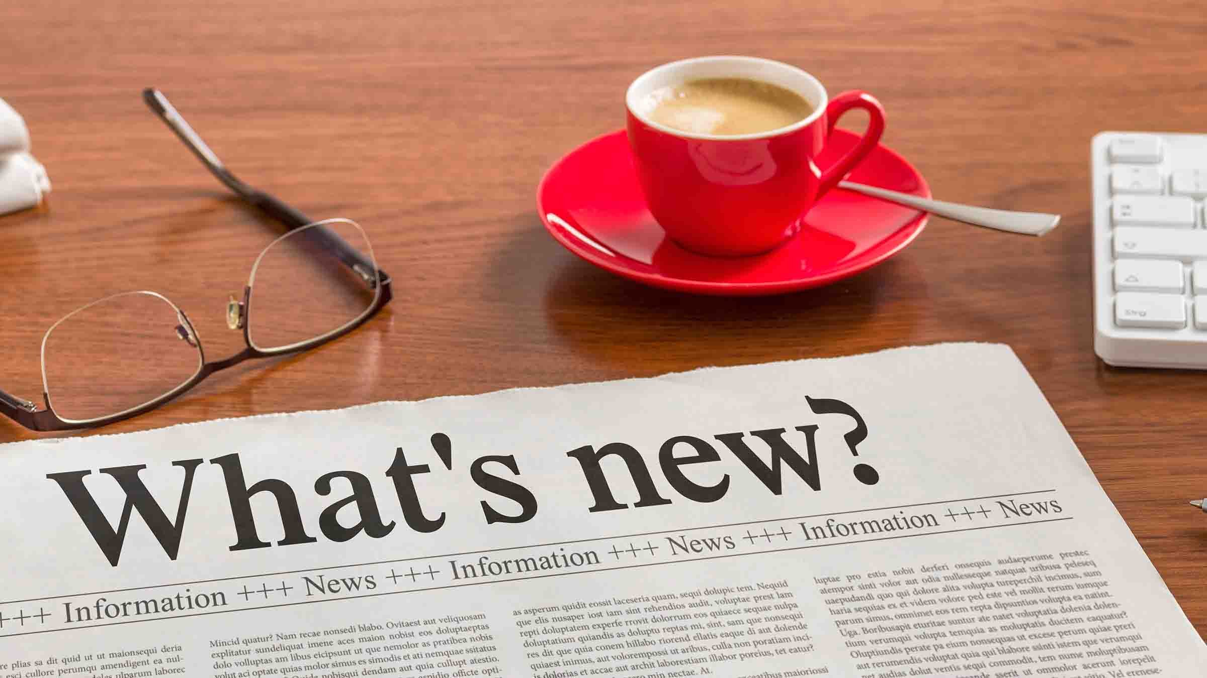 A newspaper laying on a table with red coffee cup and reading glasses.