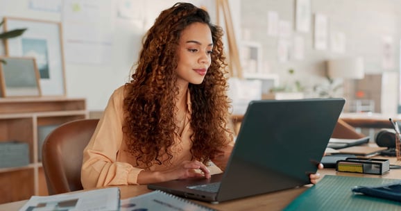 Woman sits at her desk with a laptop.