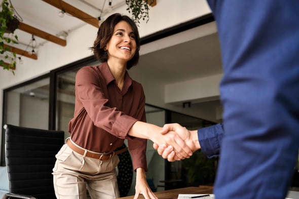 Woman stands from desk to shake hands with another person.