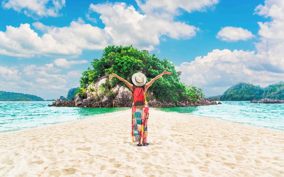 A person stand with their back to the camera dressed in vacation attire on a beautiful island surrounded by water.